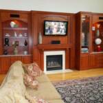 This Cherry wall-to-wall entertainment center is finished in our Japanese Sienna stain.  It features lighting, glass shelving, and marble countertops, built in speakers, surrounding an existing fireplace.

